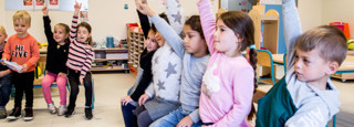 Gretige Kleuters Op Een Bank In De Klas Met Handjes In De Lucht Rh
