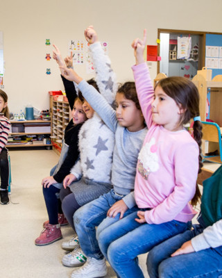 Gretige Kleuters Op Een Bank In De Klas Met Handjes In De Lucht Rh